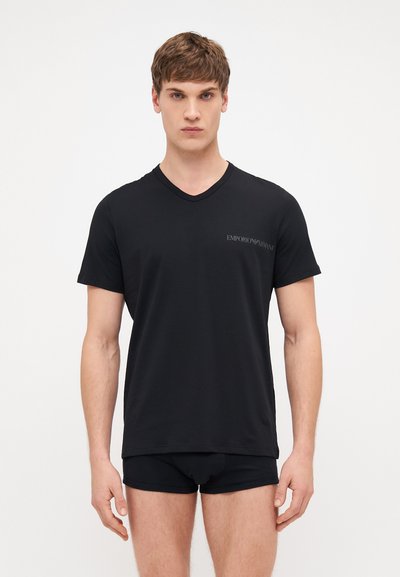 Černé tričko s krátkým rukávem ve tvaru V vyrobené z hladké tkaniny, s malým logem Emporio Armani na levé části hrudi. Nosené s černými šortkami.