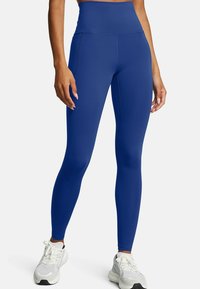 Leggings blu a vita alta realizzati in materiale elasticizzato, con cuciture piatte e un design aderente. Indossati con scarpe da ginnastica bianche.