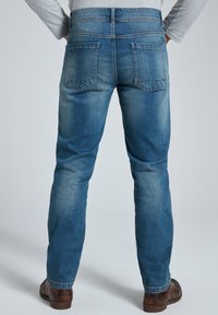 Vaqueros de mezclilla azul con un diseño de pierna recta, que presentan dos bolsillos traseros y un lavado descolorido, combinados con zapatos marrones.