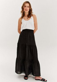 Čierna tiered maxi sukňa vyrobená z ľahkej látky, s elastickým pásom a vo voľnom strihu. Nosená s bielym tielkom a čiernymi sandálmi.