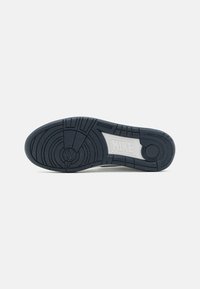 Suola di sneaker Nike, gomma nera con motivi di battistrada circolari e accenti bianchi. Presenta il marchio nell'area della suola intermedia. Texture liscia.