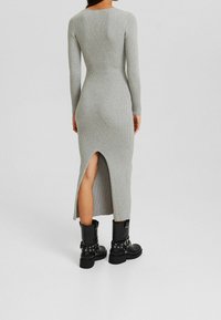 Graues geripptes Langarmkleid mit einem Schlitz hinten, kombiniert mit schwarzen kniehohen Stiefeln mit Schnallen- und Nietenverzierung.