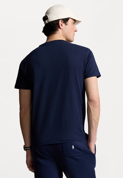 Camiseta de algodón azul marino de manga corta, con cuello redondo y un pequeño logo blanco cerca del dobladillo. Combinada con pantalones a juego y una gorra.