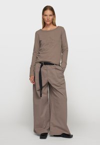 Chemise marron à manches longues avec des détails brodés, assortie à un pantalon large beige et une ceinture noire, présentant une coupe décontractée et une texture lisse.