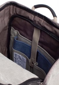 Interno di una borsa in tessuto grigio con vari scomparti. Include tasche viola scuro, grigie e blu, oltre a un'etichetta con le istruzioni per la cura.