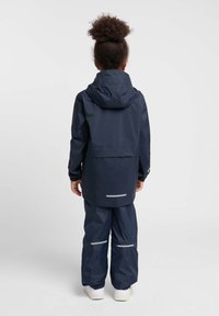 Navyblaue wasserdichte Jacke und Hose mit elastischen Bündchen, verstellbarem Kapuzenrand und reflektierenden Akzenten, von hinten betrachtet.