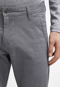 Graue Baumwollhose mit flacher Vorderseite, Gürtelschlaufen und Seitentaschen, mit feiner Textur und einem einzelnen Knopfverschluss an der Taille.