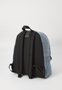 Sac à dos en denim gris avec base et bretelles en tissu noir. Il présente des bretelles rembourrées et une boucle de suspension en haut ; design minimaliste.