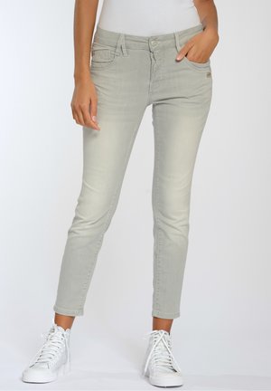 Jeans de mezclilla gris claro, diseño ajustado con cinco bolsillos, cierre de botón y costuras en contraste, combinados con zapatillas blancas.