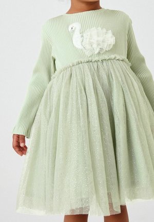 Enfant portant une robe rayée vert clair avec une jupe en tulle pailleté et une appliqué de cygne avec des ailes en tissu superposées sur la poitrine.