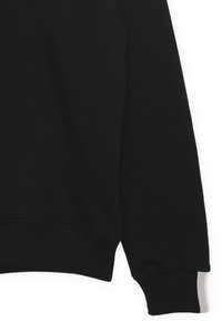 Felpa nera con orlo e polsini a costine. Presenta un'accenno grigia sul polsino. Realizzata in un morbido tessuto testurizzato.