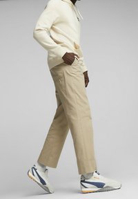 Cremiger Hoodie, beiger Pants und weiße Sneakers mit marineblauen Akzenten. Kapuzen-Design, Fronttasche und lässige Passform mit umgeschlagenen Säumen an den Pants.
