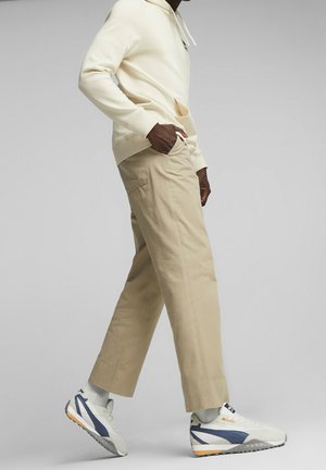 Felpa crema con cappuccio, pantaloni beige e sneakers bianche con accenti blu navy. Design con cappuccio, tasca frontale e vestibilità casual con polsini arrotolati sui pantaloni.