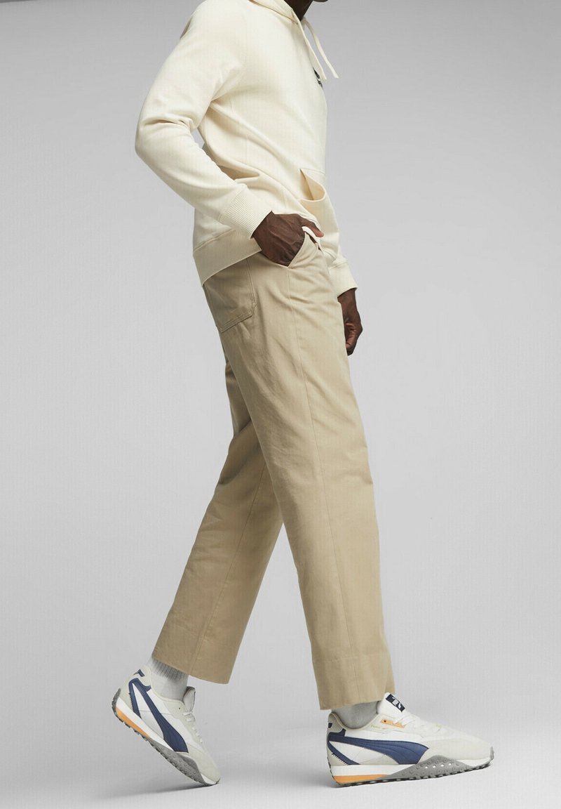 Cremiger Hoodie, beiger Pants und weiße Sneakers mit marineblauen Akzenten. Kapuzen-Design, Fronttasche und lässige Passform mit umgeschlagenen Säumen an den Pants.