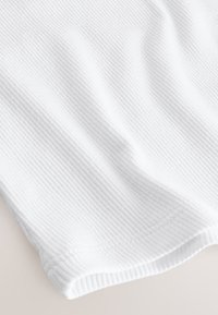 Tissu blanc côtelé montrant la texture et les coutures le long de l'ourlet, avec des plis subtils créant des ombres douces.