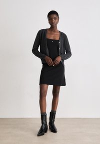 Black dress with square neckline, layered with a dark gray cardigan. Glossy black ankle boots with ribbed gray accents complete the outfit.