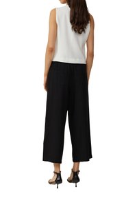 White ribbed sleeveless top paired with black wide-leg pants. The pants feature back pockets and a relaxed fit, complemented by black high-heeled shoes.