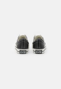 Črne platkaste superge z gumijastimi podplati, belim šivom in kontrastnimi belimi podplati. Opremljene z blagovno znamko "Converse All Star" na peti.