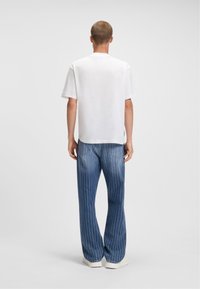 Camiseta blanca de manga corta con corte recto, combinada con pantalones de denim azul que presentan rayas verticales blancas y un corte ligeramente relajado.