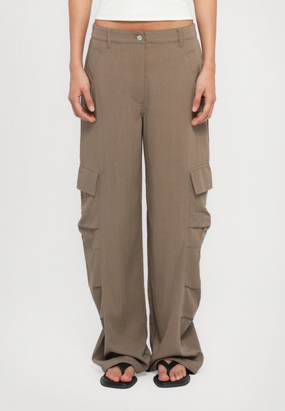 Pantalons cargo en tissu brun clair, présentant une coupe décontractée, de grandes poches latérales et une jambe droite. Portés avec des tongs.