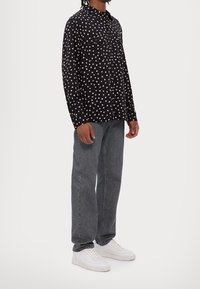 Černá košile na knoflíky s bílým hvězdným vzorem, dvěma předními kapsami, dlouhými rukávy; spárováno se šedými džíny a bílými teniskami.