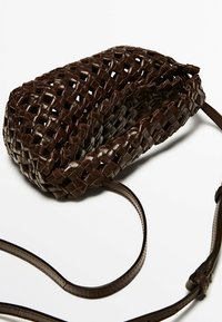 Flätad brun läderväskan med rundad form, lång rem och texturerad yta. Har intrikata flätningar och en minimalistisk design.