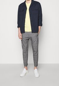 Granatowa kurtka na guziki, jasnżółty t-shirt, szare spodnie w wzory oraz białe trampki dopełniają strój.