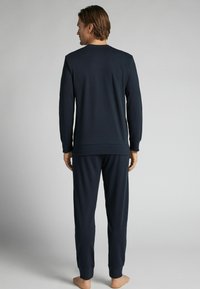 Námořnický volnočasový set, který zahrnuje dlouhý rukáv a kalhoty, vyrobený z měkkého materiálu s žebrovanými manžetami a páskem. Hladká textura.