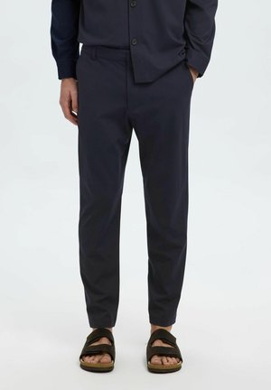 Pantalon bleu marine à coupe slim, avec une texture lisse, des poches latérales, associé à des sandales marron avec des sangles réglables.