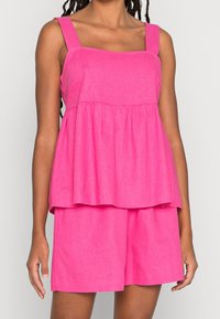 Haut péplum en lin rose avec bretelles larges, encolure carrée et coupe ample, associé à un short assorti, présentant une texture douce.