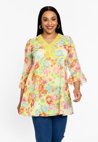 Bloemen tuniek met een gele achtergrond, versierd met levendige bloemen in roze, oranje en blauw. V-hals ontwerp met decoratieve stiksels en klokmouwen.