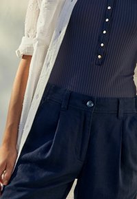 Granatowe prążkowane body z perłowymi guzikami, połączone z luźnymi lnianymi spodniami w granatowym kolorze, posiadającymi guziki z przodu i boczne kieszenie. Biała teksturowana koszula na płaszcz.