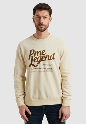 Crème-kleurige sweatshirt met een ronde hals. Heeft vetgedrukte bruine tekst en een grafische print. Zacht materiaal, geribbelde manchetten en zoom.