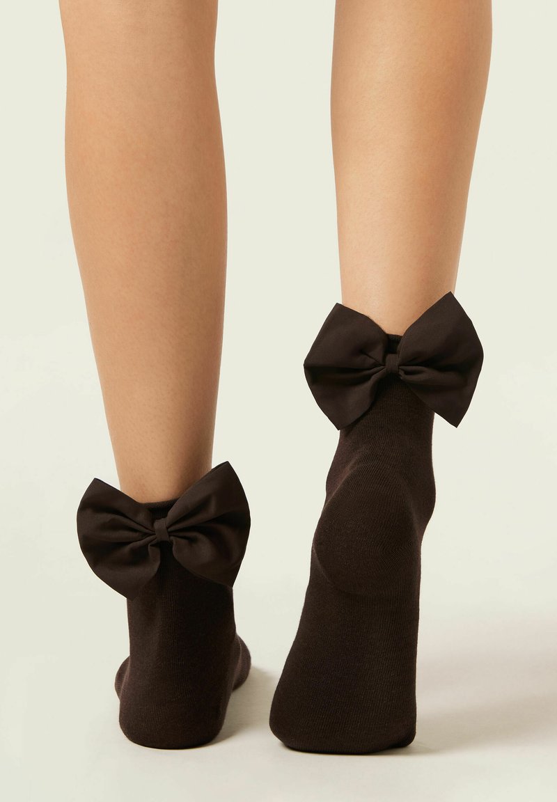 Bruna ankelsockor med stora satinrosetter vid hälarna. Materialet verkar mjukt, med en slät yta och enkel design.