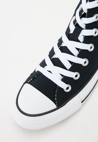 Svart canvas sneakers med hvit gummisåle og tåhette, med hvite snørebånd og sølvfargede blonder, teksturert stoff og klassisk design.