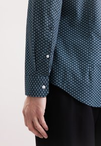 Camicia blu scuro con un motivo circolare in azzurro, con polsini abbottonati e orlo leggermente curvato. Tessuto morbido.