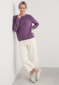 Lila strukturerad stickad tröja med rund halsringning, i kombination med gräddvit vida byxor och ljusgrå sneakers. Minimalistisk design utan mönster.