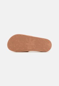 Semelle en caoutchouc beige avec un motif de grip texturé et un logo en relief. Forme incurvée avec une finition lisse et des bords renforcés.