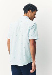 Camicia a maniche corte in azzurro chiaro con un sottile motivo a righe, caratterizzata da piccoli motivi di palme e un design del colletto casual.