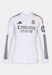 Maglia a maniche lunghe bianca con accenti neri e gialli, presenta il logo "Emirates Fly Better" e il simbolo del Real Madrid, realizzata in materiale sintetico leggero.
