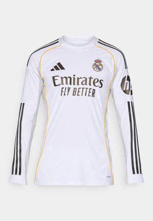 Maillot à manches longues blanc avec des accentuations noires et jaunes, portant le logo "Emirates Fly Better" et l'écusson du Real Madrid, fabriqué en matériau synthétique léger.