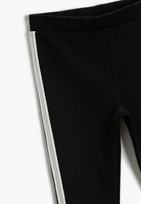 Leggings negras con un diseño ajustado, que presentan una franja lateral en gris. Fabricadas con un material suave y con una cinturilla elástica para mayor comodidad.
