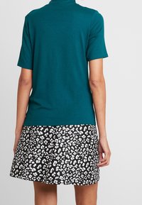 Teal kortærmet top parret med en sort-hvid leopardmønstret skaternederdel. Stoflet ser glat og let ud.