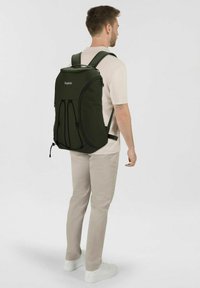 Dunkelgrüner Rucksack mit strukturiertem Design, verstellbaren Trägern und einem zentralen Reißverschluss. Verfügt über elastische Schnüre auf der Vorderseite für zusätzliches Stauraum.