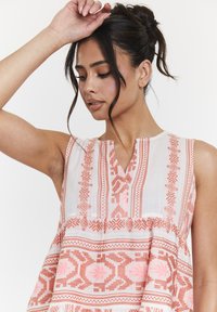 Leichtes, ärmelloses Kleid in Creme mit rosa geometrischen Mustern, das eine V-Ausschnittlinie und einen strukturierten Stoff aufweist. Der ausgestellte Schnitt betont die Silhouette.