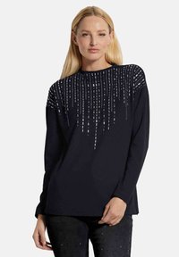 Zwarte longsleeve top met een gestructureerde hoge hals en een ontwerp van verticale metallic accenten langs de borst, wat visuele textuur toevoegt.