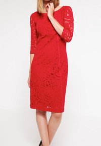 Röd spetsklänning med trekvartslånga ärmar, invecklat blommönster, åtsittande siluett och knälång klippning. Slät textur med synliga sömmar.