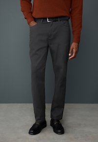 Szare spodnie o prostym kroju z bocznymi kieszeniami, zestawione z czarnymi butami. Materiał jest gładki z lekkim połyskiem.