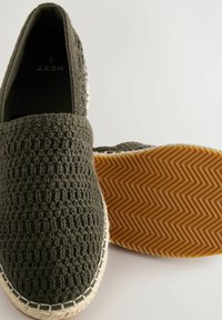 Grå vævede slip-on sko med en tekstureret overdel, hvide syninger og en gummisål med fiskebensmønster.