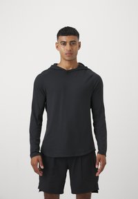 Schwarzes Langarmshirt mit Kapuze, aus leichtem Material hergestellt. Glatte Textur, figurbetontem Schnitt, mit Raglanärmeln und geschwungenem Saum.